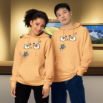 Modelos masculino y femenino usando la sudadera Splash Paint amarilla en una galería o museo, demostrando su versatilidad como producto unisex y su capacidad para expresar el talento artístico en un estilo casual y urbano.